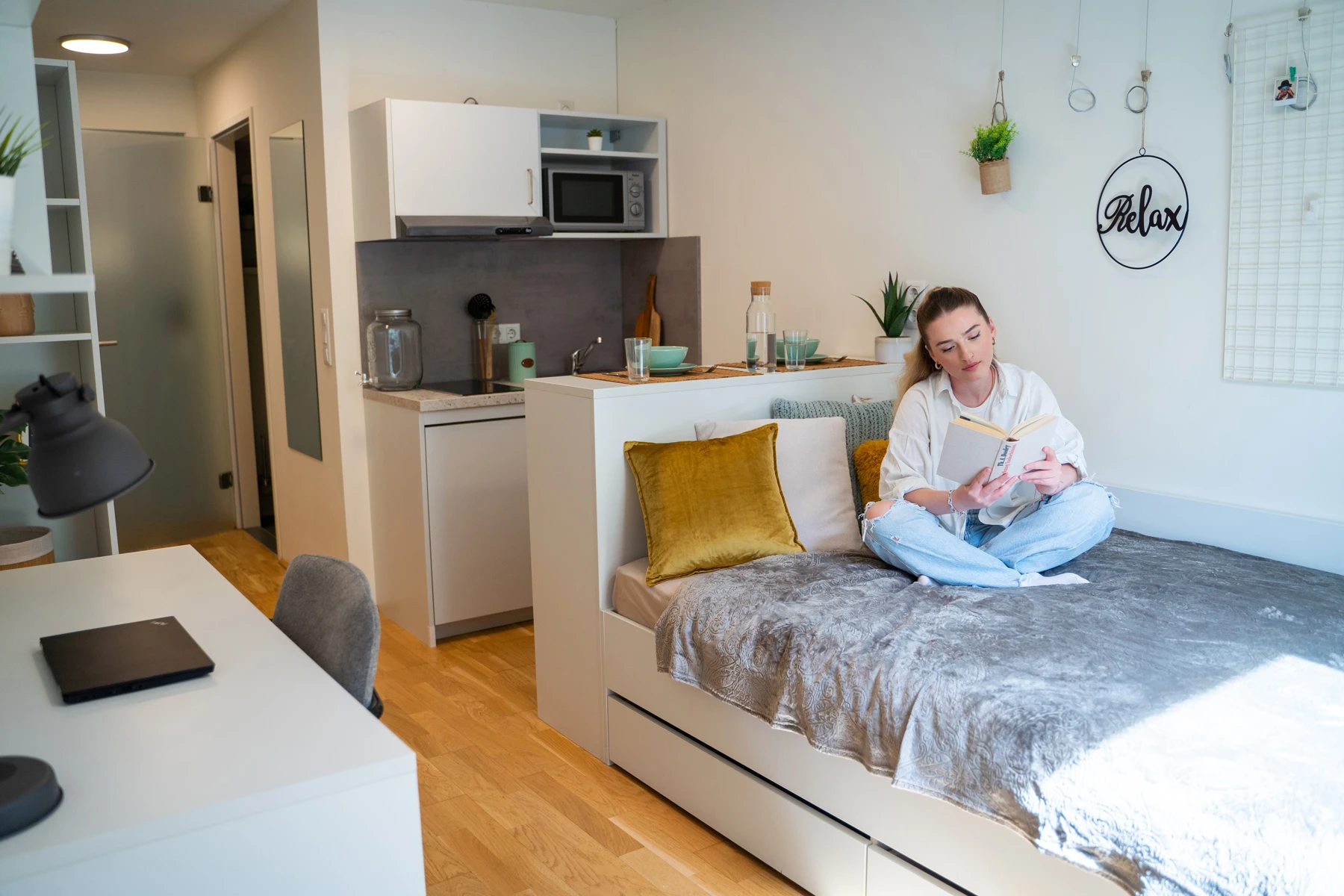 Junge Frau liest in ihrem modernen, kleinen Apartment. Helle, gemütliche Atmosphäre mit integrierter Küche und Schlafsofa.